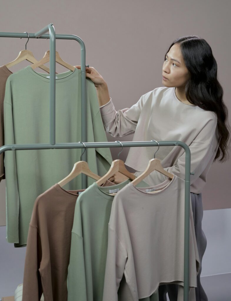 A rack of neutral-toned outfits with basics like jeans, white shirt, trench coat.